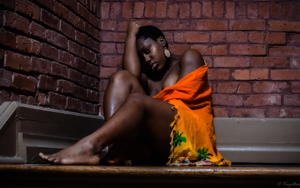 Black woman sitting in corner with brick walls