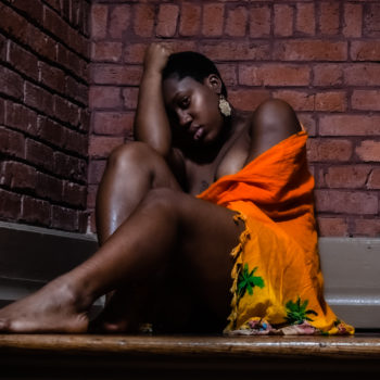 Black woman sitting in corner with brick walls