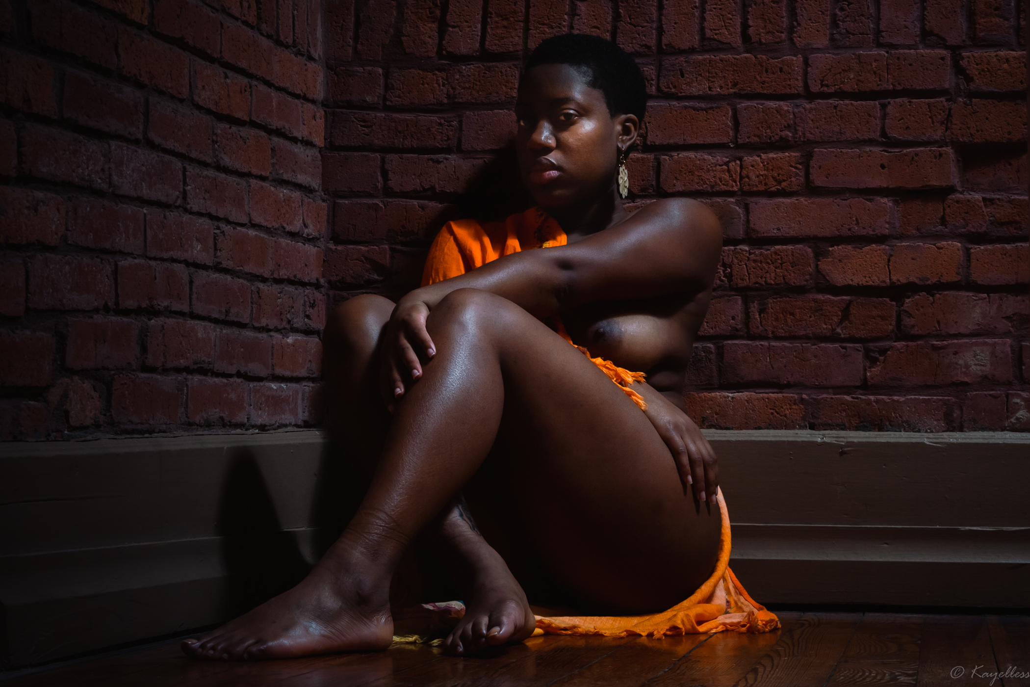 Black woman sitting in corner with brick walls
